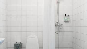 A bathroom with a toilet, shower, and a small shelf with toiletries.