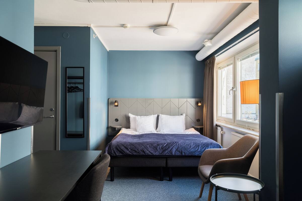 A hotel room with a bed, a desk, a chair, a TV, and a window with curtains.