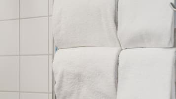 A metal towel rack with three folded white towels against a tiled wall.