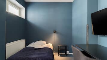 Een slaapkamer met een bed, nachtkastje, stoel en een televisie aan de muur.