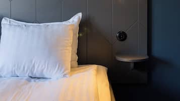 A neatly made bed with white linens, a headboard with geometric patterns, a bedside table with a light, and a power outlet on the wall.