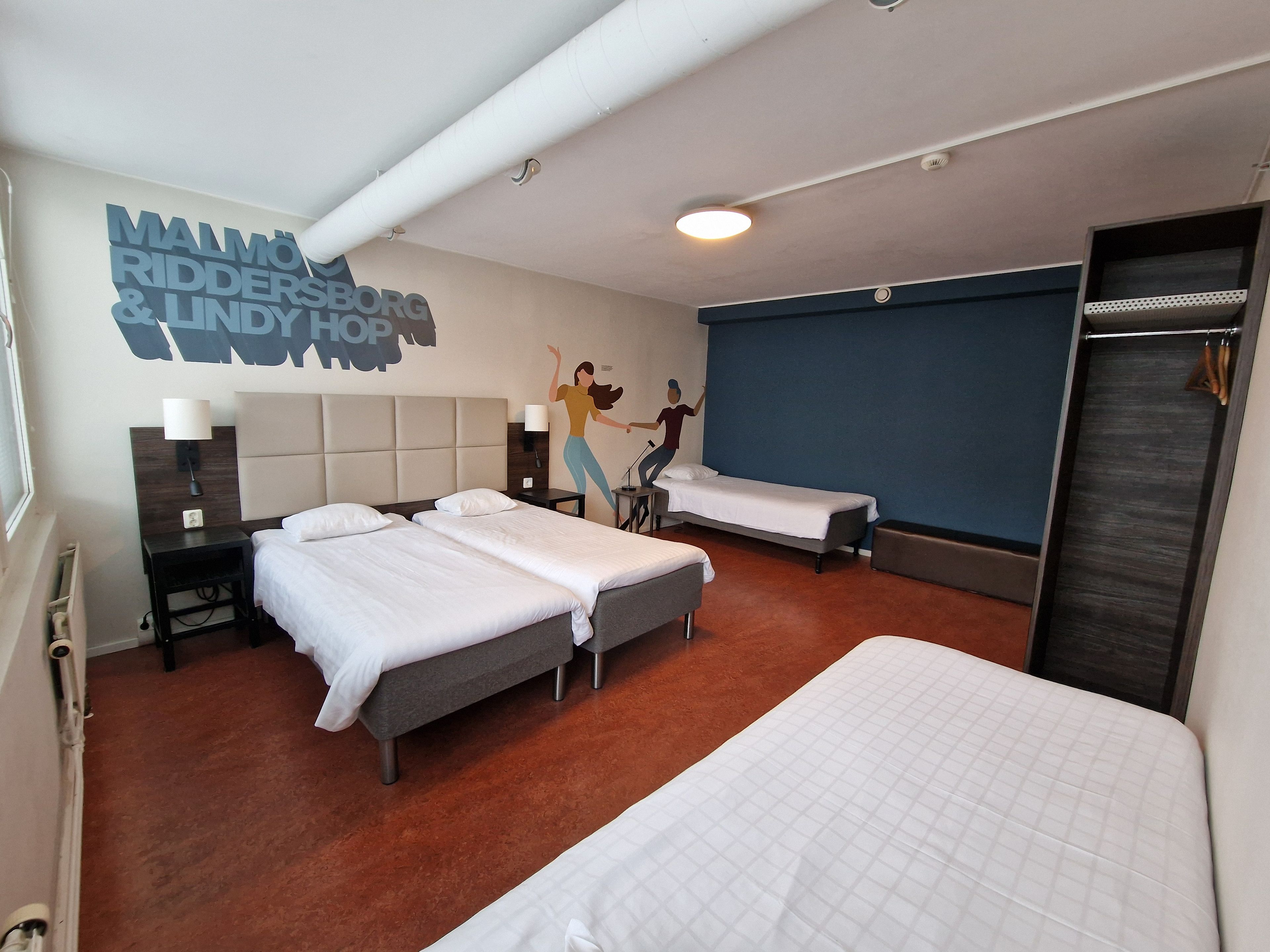 A hotel room with two beds, a wall mural, a wardrobe, and a bathroom.