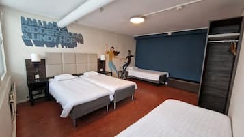 A hotel room with two beds, a wall mural, a wardrobe, and a bathroom.