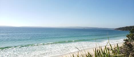 A beach with clear blue water, sandy shore, and distant hills.