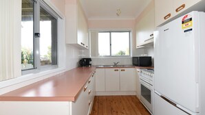 Une cuisine de taille réduite avec des meubles blancs, un plan de travail en bois, un évier, un four à micro-ondes et un réfrigérateur.