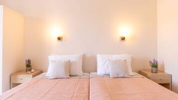 A double bed with a pink quilt, two white pillows, and a small plant on a bedside table.