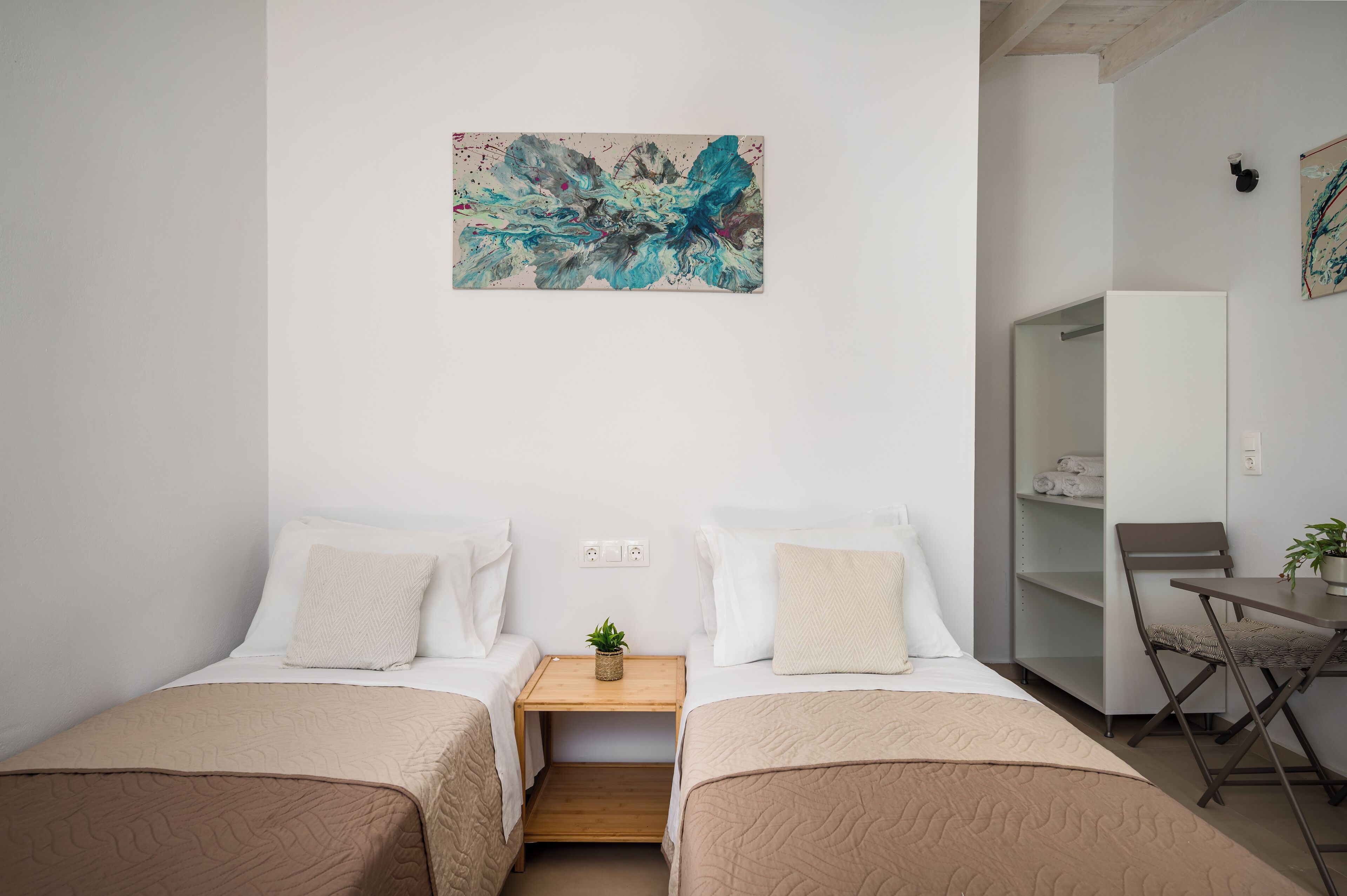 A modern hotel room with two beds, a small table with a plant, and a large abstract painting on the wall.