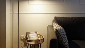 Ein Zimmer mit einer Lampe auf einem kleinen Tisch, einem Buch und einem Kissen auf einer Couch.