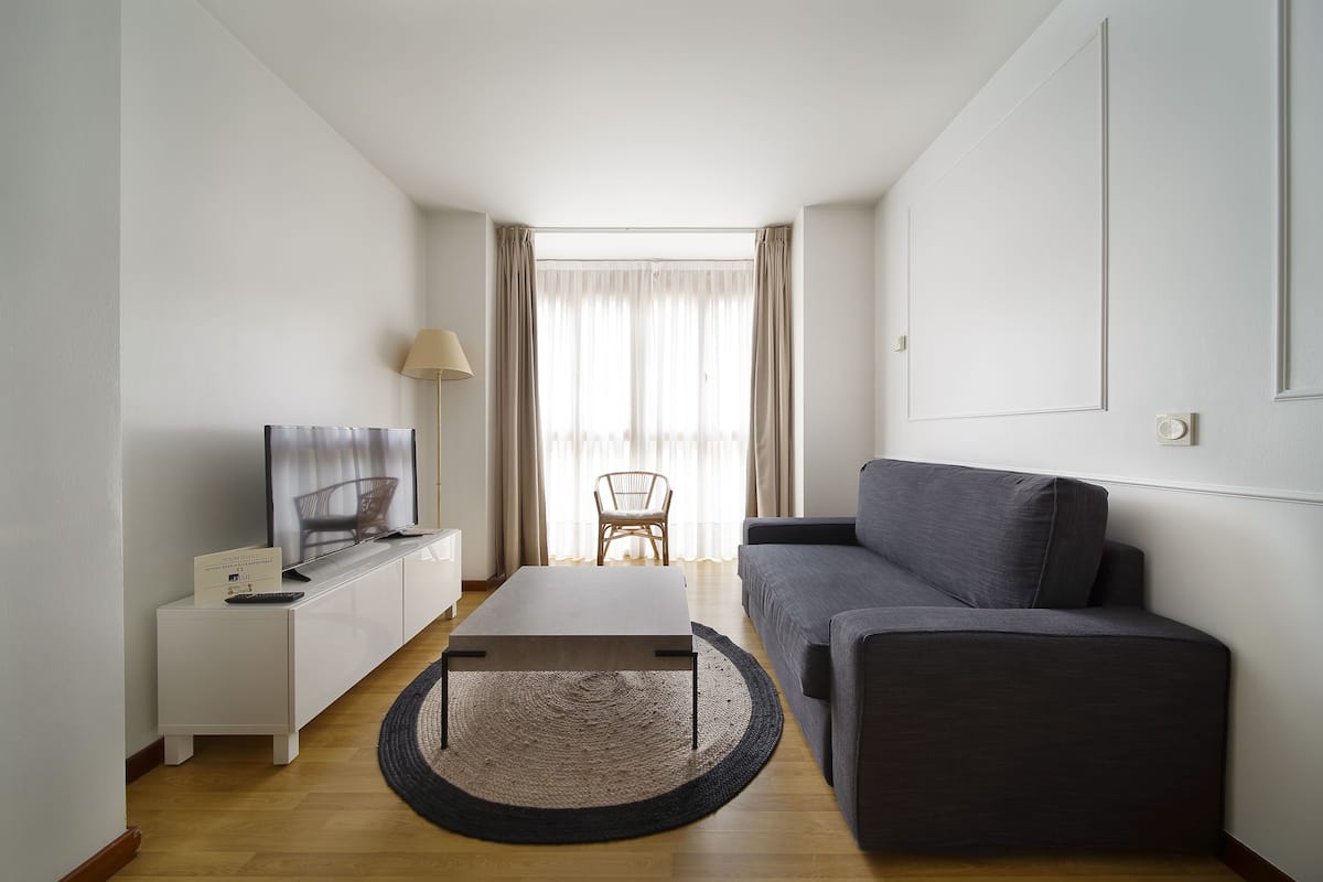 Ein modernes Wohnzimmer mit einer Couch, einem Couchtisch, einem Fernseher und einem Sessel.