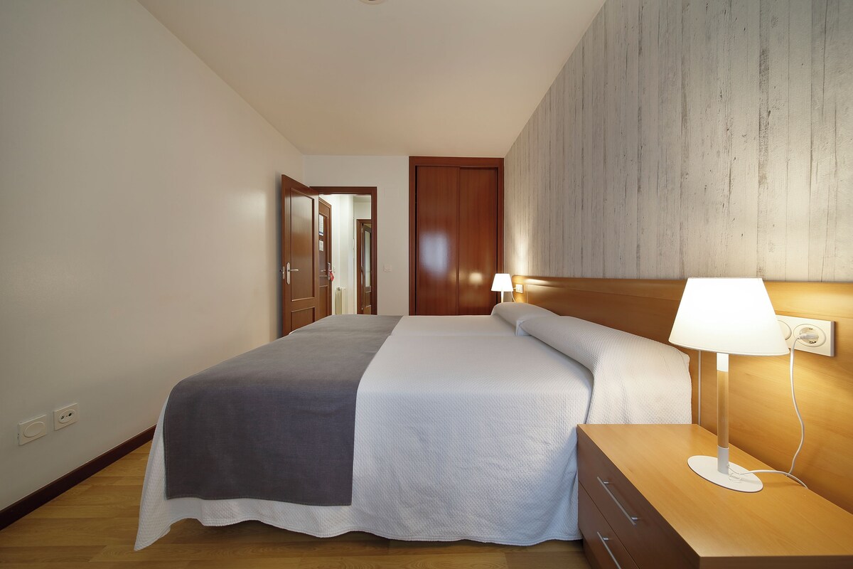 A bedroom with a bed, bedside tables, and a wall-mounted lamp.