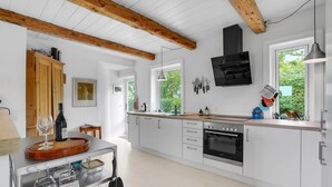 Een moderne keuken met witte kasten, een houten plafond, een inbouwoven en een raam met uitzicht op groen.