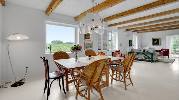 Een ruime eethoek met een houten tafel en stoelen, een kroonluchter en uitzicht op het omliggende landschap.
