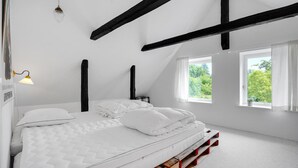 Een slaapkamer met een bed, twee ramen, een lamp en uitzicht op groen.