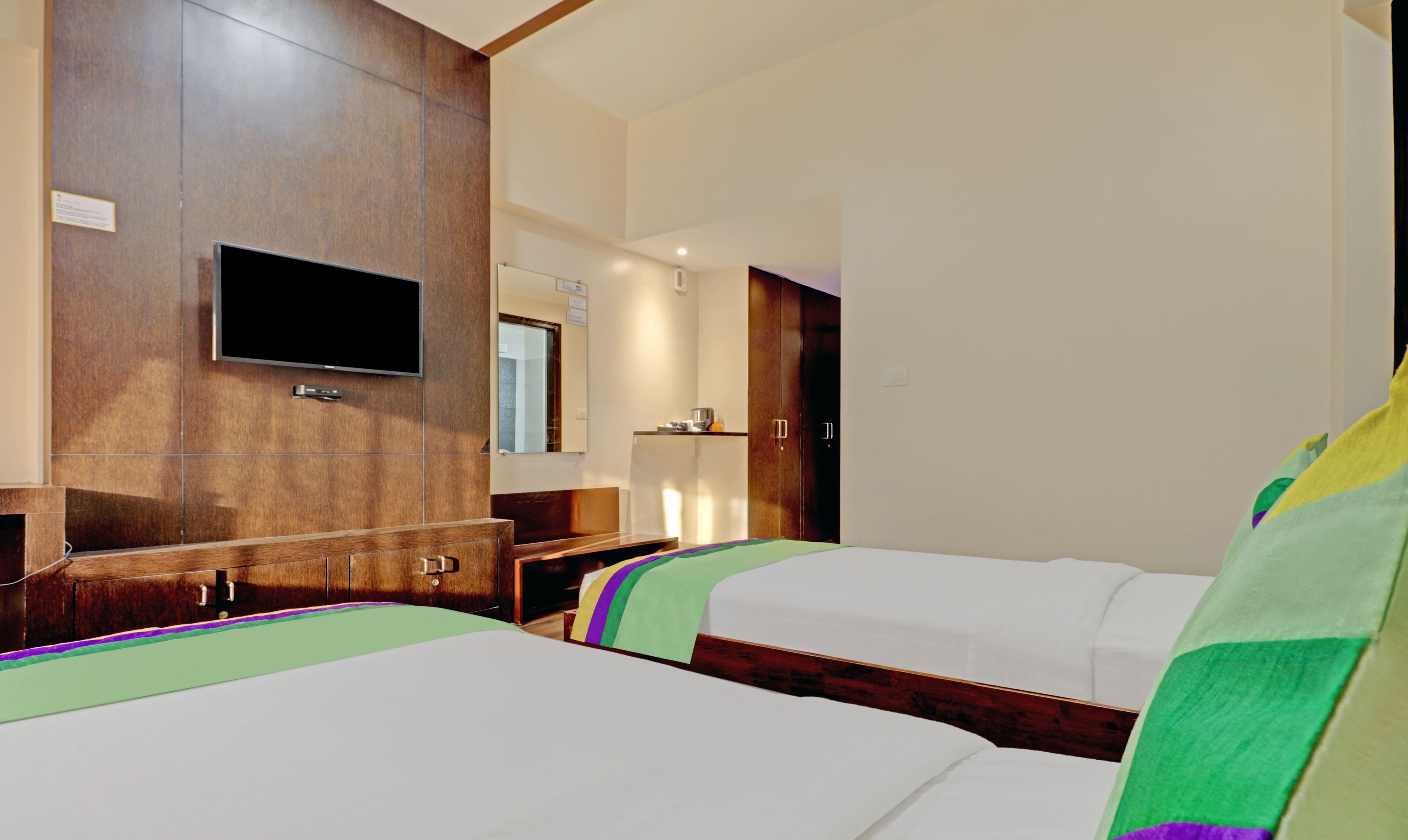 Habitación de hotel con dos camas, un televisor montado en la pared, un armario de madera y un escritorio pequeño con una silla.