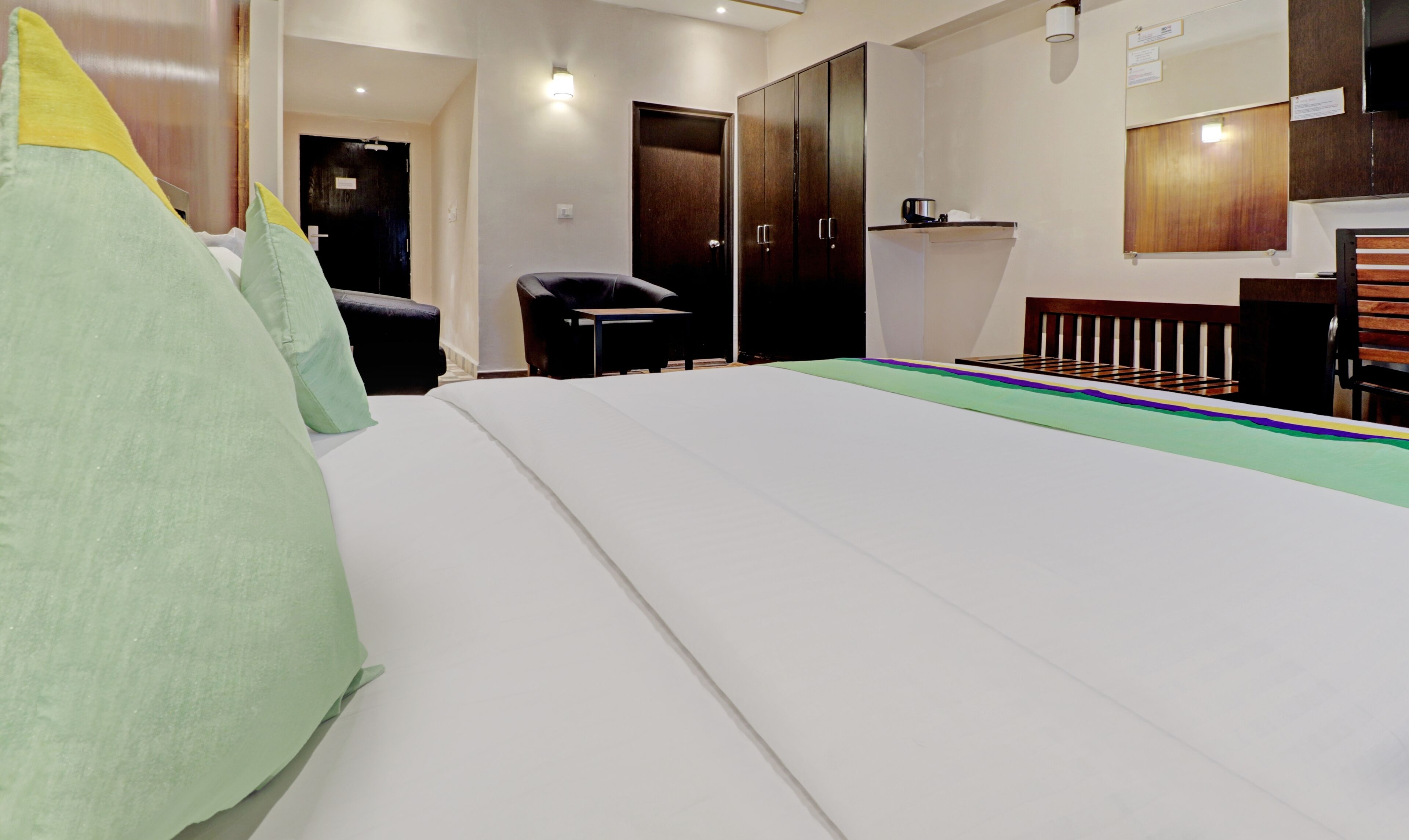 A hotel room with a large bed, a desk, a chair, a wardrobe, and a small kitchenette.
