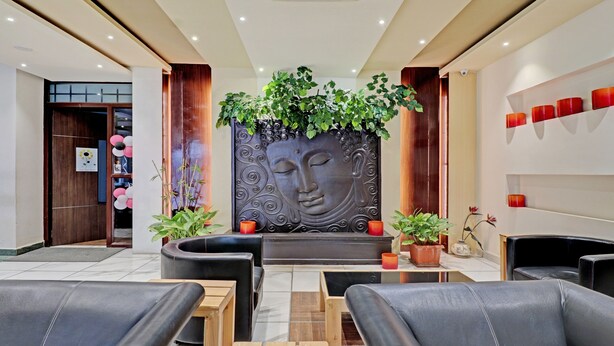 A modern lobby with leather seating, a Buddha statue, and potted plants. - Treebo Astor HSR Layout (Bengaluru)