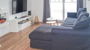 Ein modernes Wohnzimmer mit einem grauen Ecksofa, einem Flachbildfernseher, einer weißen Unterhaltungseinheit und einem kleinen runden Tisch.