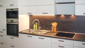 Eine moderne Küche mit weißen Schränken, einer Edelstahl-Spüle, einem eingebauten Ofen und einer Holz Arbeitsplatte.