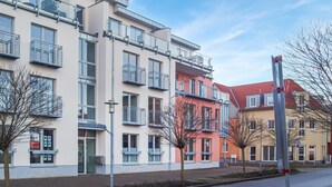 Ein mehrstöckiges Wohngebäude mit Balkonen, einer Straße davor und blauem Himmel.