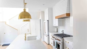 A modern kitchen with white cabinetry, a central island, a gas stove, and a stainless steel refrigerator. - Close to the beach, train and all the downtown fun! (Oceanside)