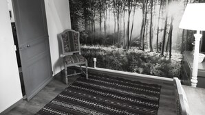 A room with a door, a chair, a patterned rug, and a forest mural on the wall.