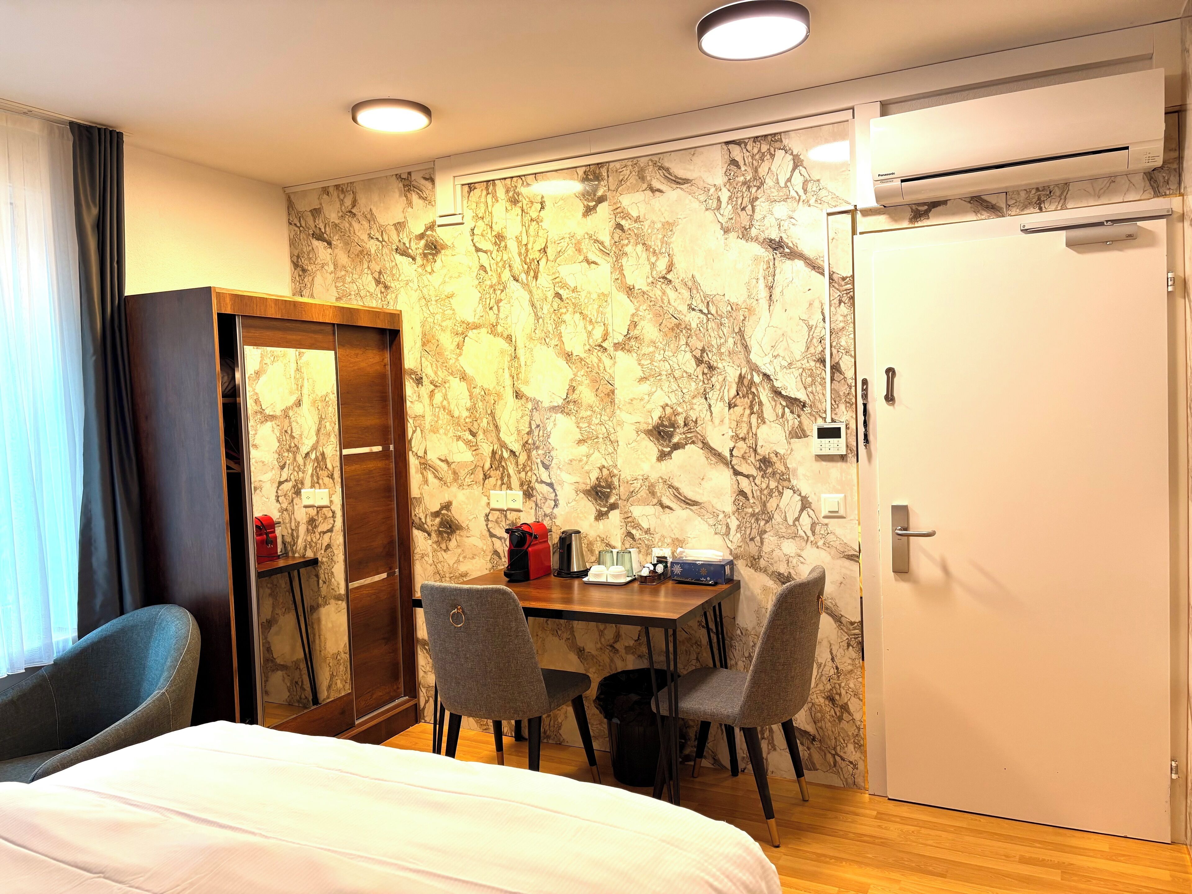 Une chambre d’hôtel comprenant un lit, un bureau, deux chaises, une armoire et un appareil de climatisation.