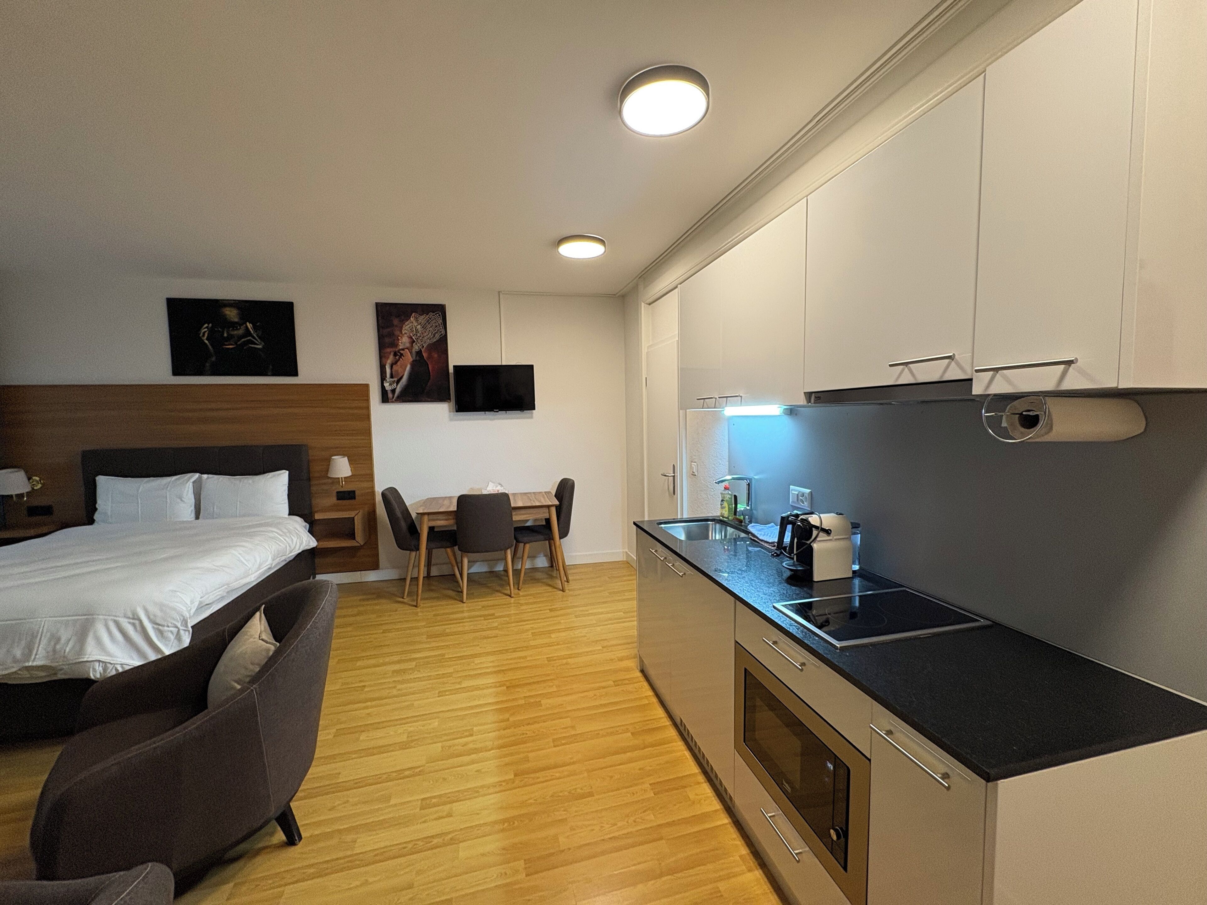 Quarto de hotel compacto com uma cama, um pequeno sofá, uma mesa de jantar e uma cozinha compacta.