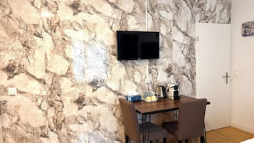 A room with a marble-patterned wall, a mounted TV, a dining table with chairs, and a bed.