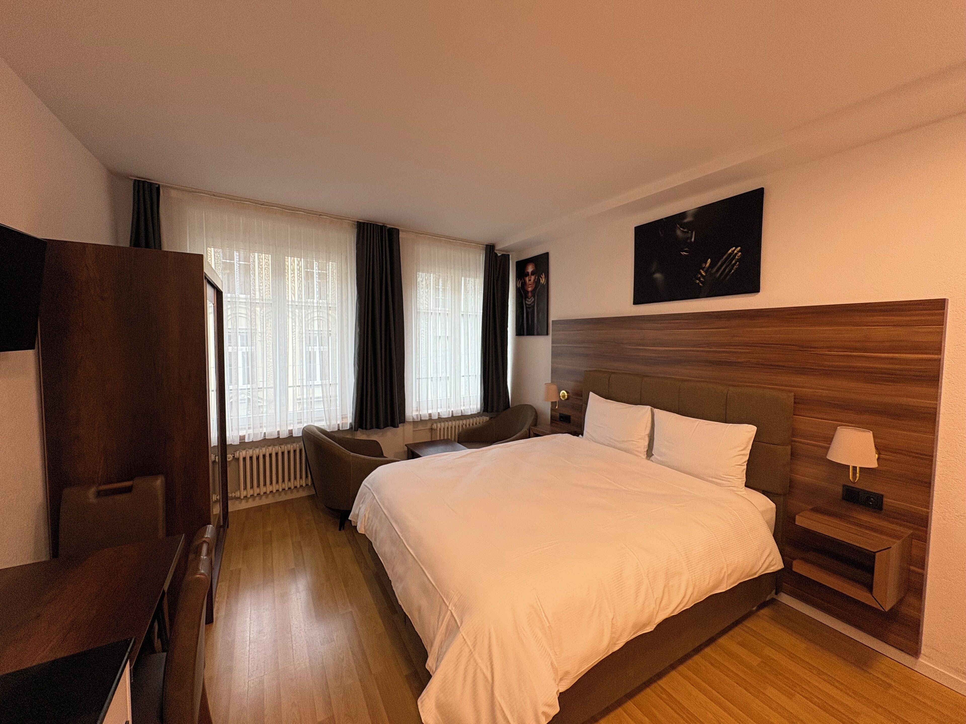 Una habitación de hotel con una cama grande, un escritorio, una silla y un ventanal con cortinas.