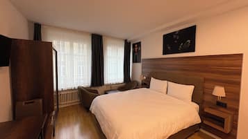 Una habitación de hotel con una cama grande, un escritorio, una silla y un ventanal con cortinas.