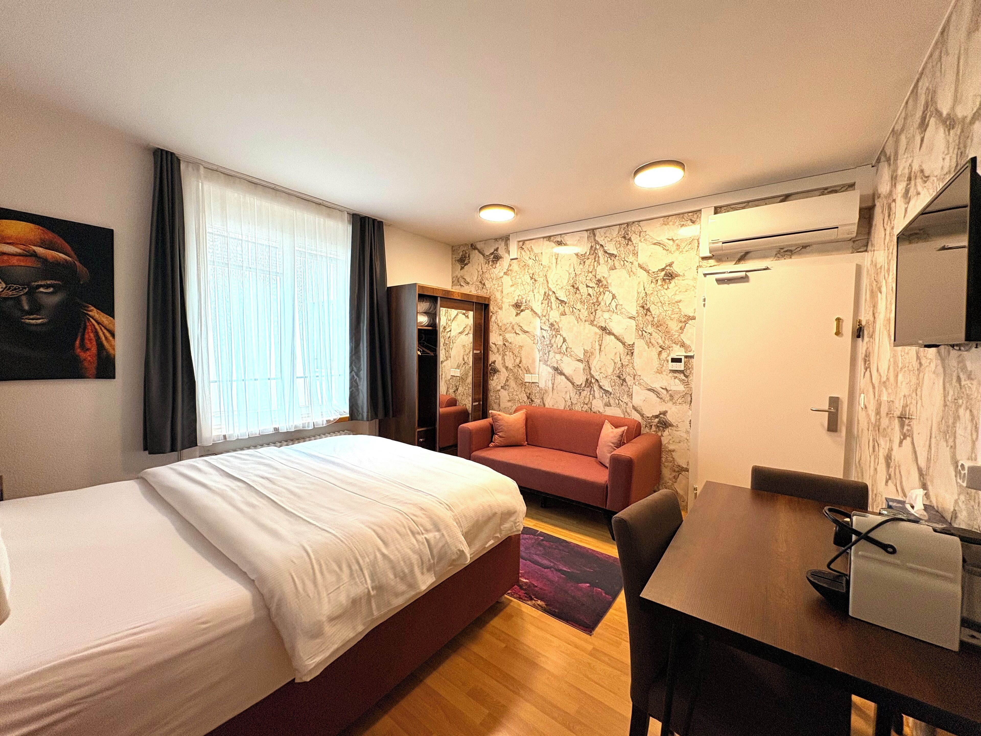 A hotel room with a bed, a sofa, a desk, and a wardrobe.