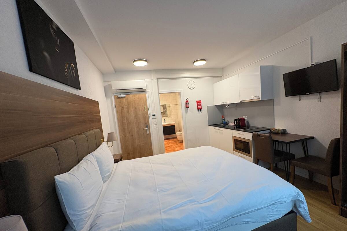 Ein Hotelzimmer mit Bett, Schreibtisch, Stuhl, Fernseher und einer Küchenzeile.