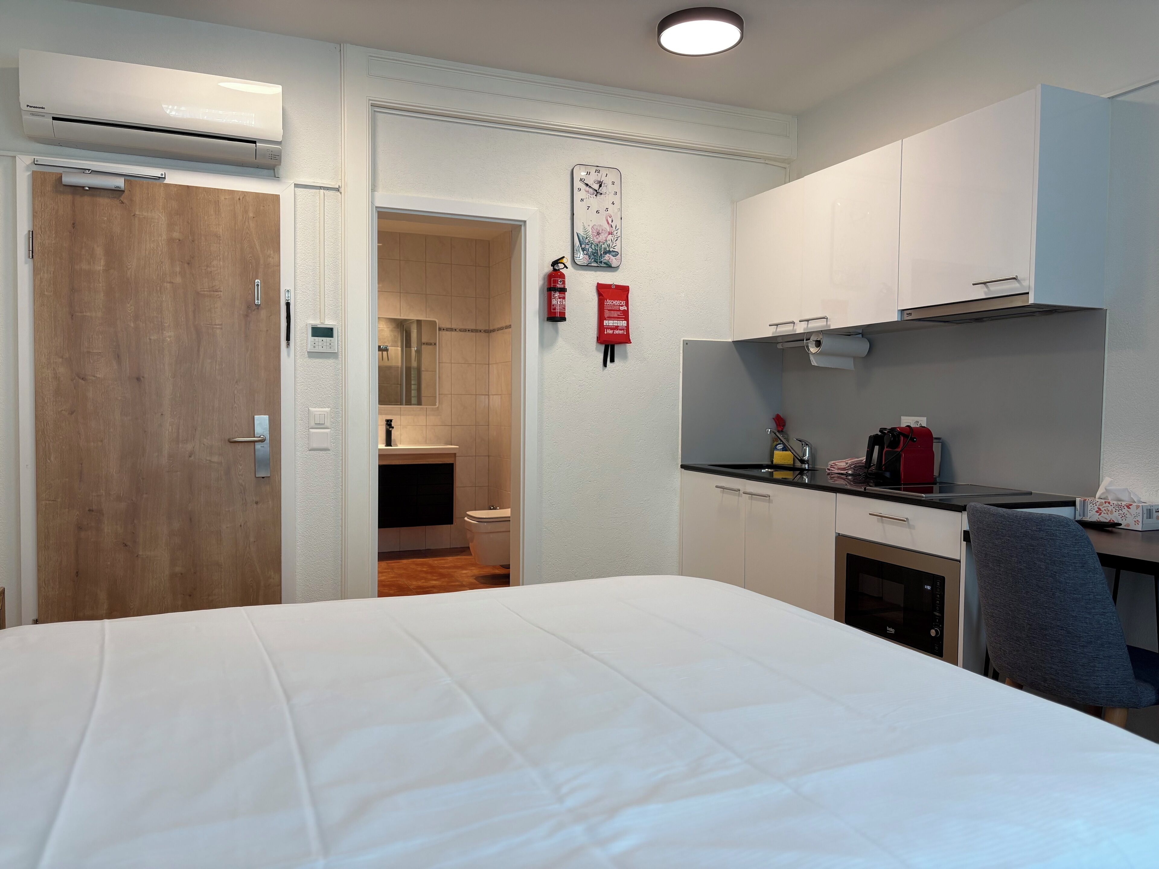 Una habitación de hotel con cama, kitchenette, baño y una puerta que da a otra habitación.