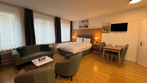 Una habitación de hotel con cama, sofá, una mesa de comedor con sillas y televisor en la pared.