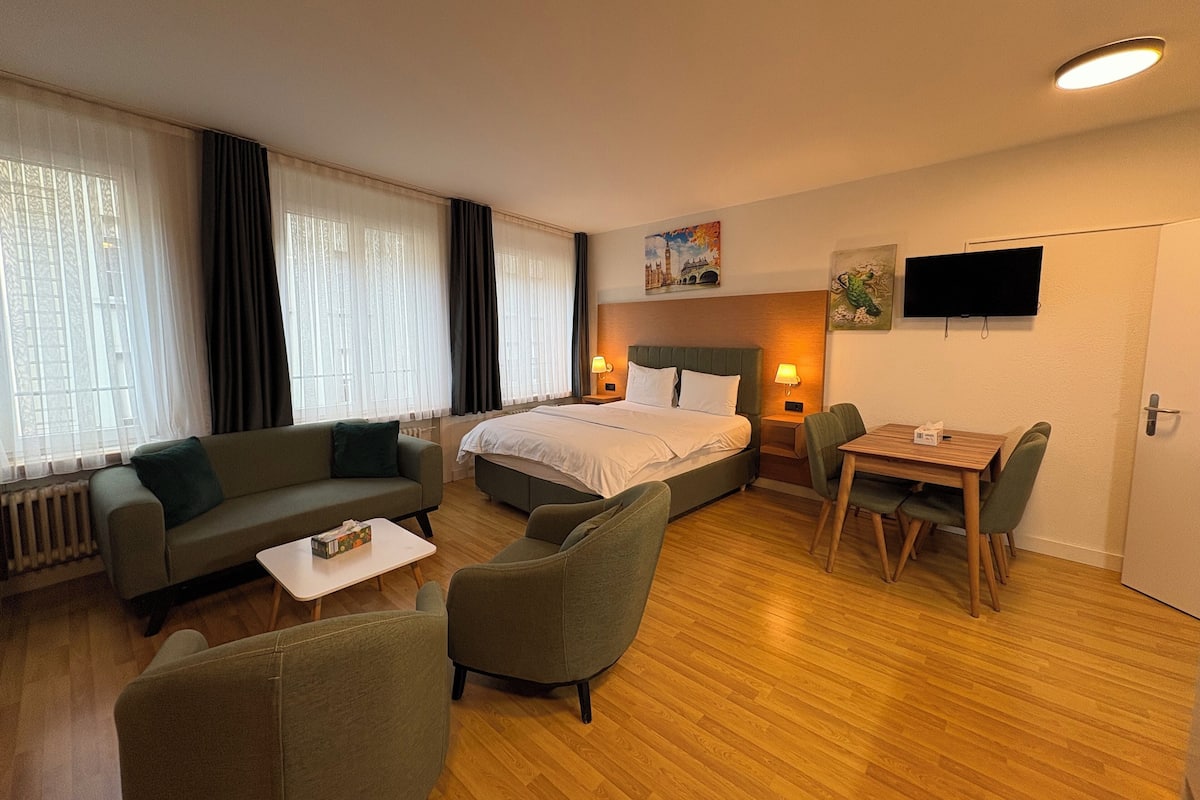 Ein Hotelzimmer mit Bett, einer Sitzecke, einem Esstisch mit Stühlen und einem Fernseher an der Wand.