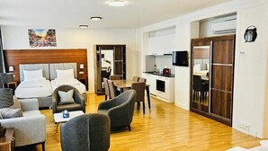 Habitación de hotel con cama, dos sillones, sofá, una mesita, televisión, zona de cocina y armario.