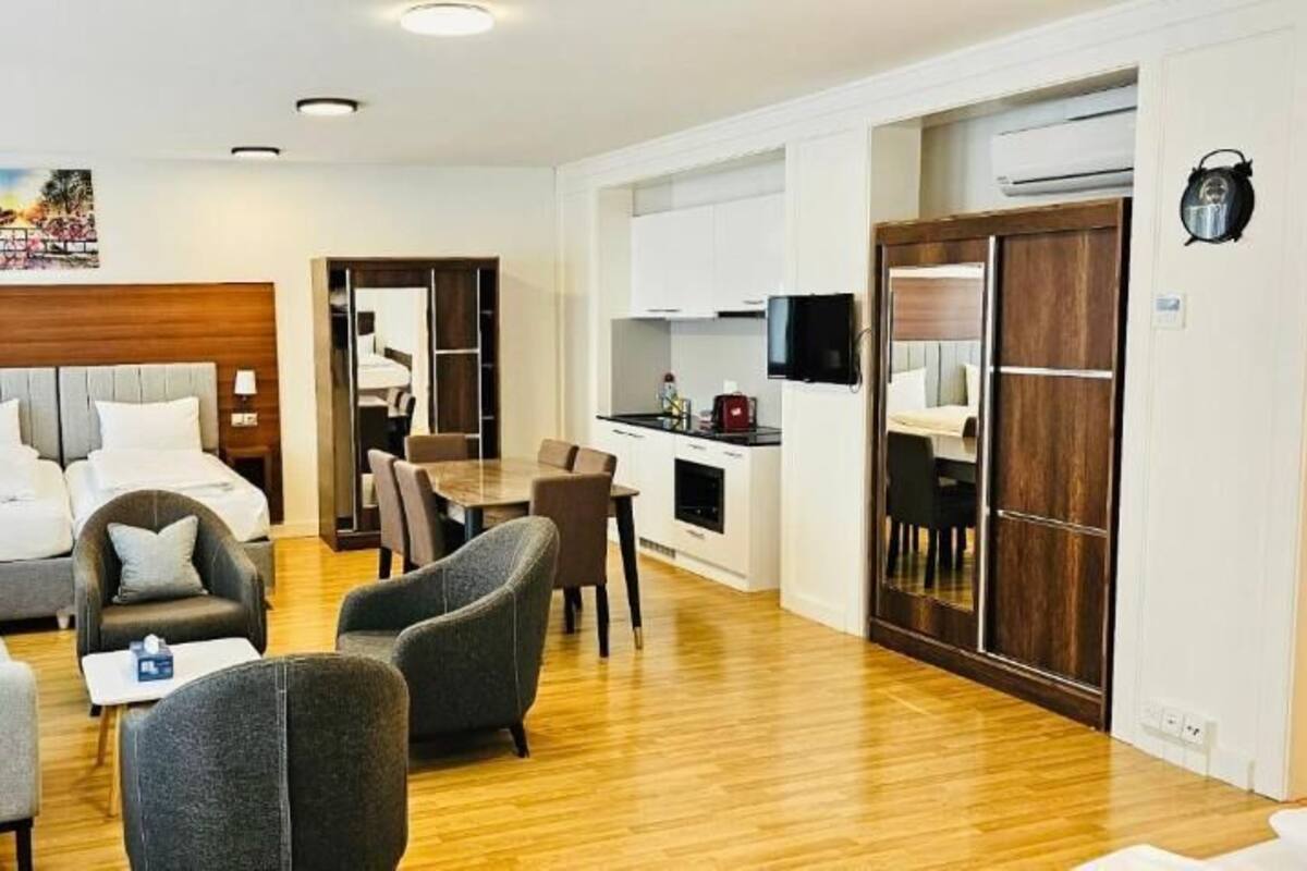 Ein Hotelzimmer mit Bett, zwei Sesseln, einer Couch, einem kleinen Tisch, einem Fernseher, einer Küchenzeile und einem Kleiderschrank.