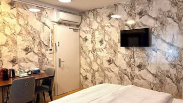 Une chambre d’hôtel comprenant un lit, un bureau avec une chaise, un appareil de climatisation, un téléviseur fixé au mur et une porte.