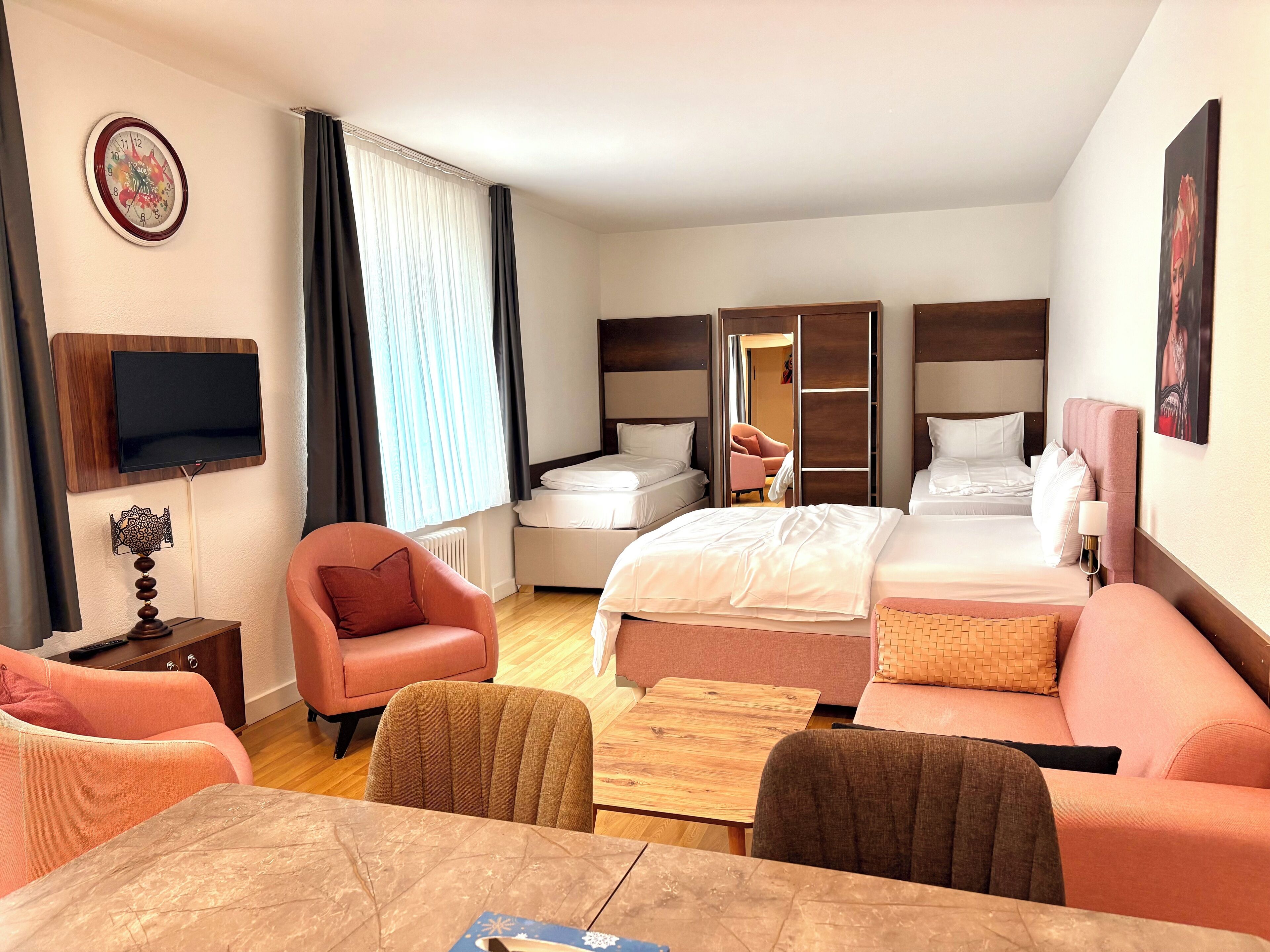 A hotel room with a bed, two bedside tables, a TV, a sofa, a chair, and a table.