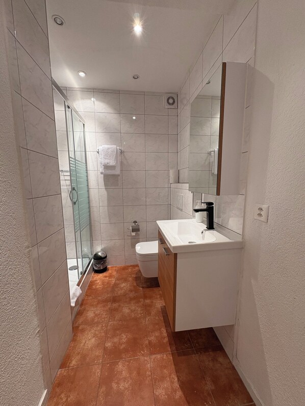 A modern bathroom with a glass shower enclosure, white tiles, and a wooden vanity.
