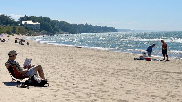 A beach with people relaxing, a house in the background, and the ocean.