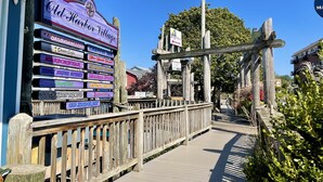 A wooden boardwalk leading to a sign for Old Harbor Village with various business names listed.