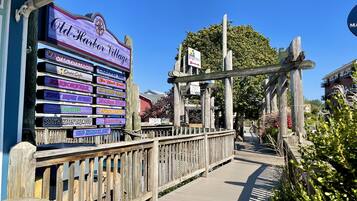 A wooden boardwalk leading to a sign for Old Harbor Village with various business names listed.