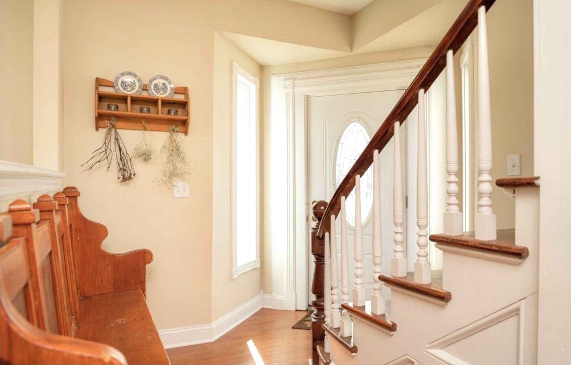 Un escalier en bois, avec des balustrades blanches, mène à une porte ornée d’un vitrail décoratif.
