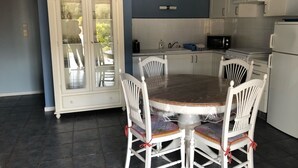 Una cocina con una mesa redonda de comedor, sillas blancas, un armario y un microondas.
