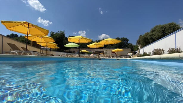Una piscina con agua azul cristalina, rodeada de sombrillas amarillas y verdes, y sillas de descanso.