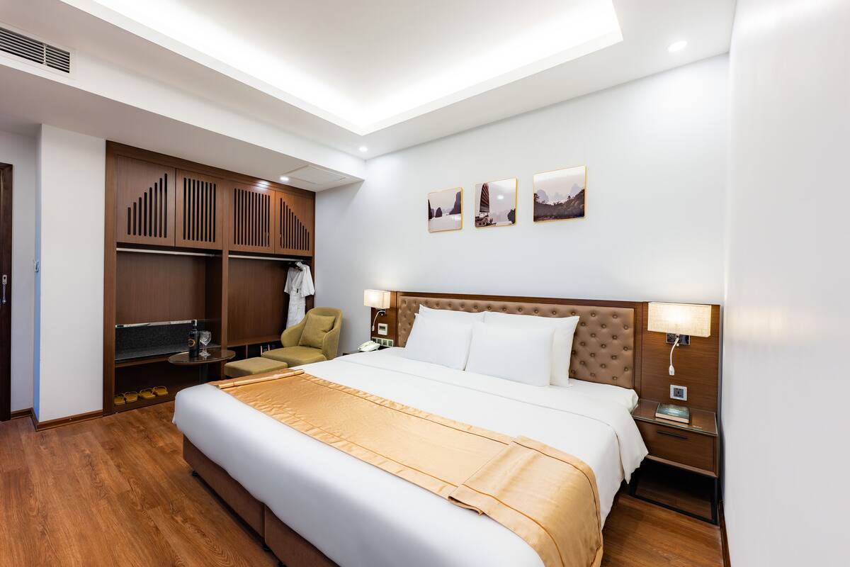 Een hotelkamer met een groot bed, een houten garderobe, een stoel en drie ingelijste foto's aan de muur.