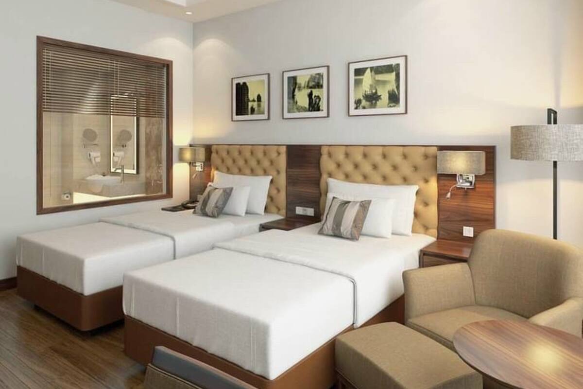 Hotelkamer met twee bedden, een bank, een stoel, een tafel en drie foto's in lijsten aan de muur.