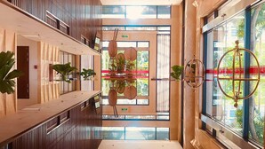 A modern hotel lobby with a central chandelier, large windows, and a glass wall offering a view of the outdoors. - Ha Long New Century Hotel (Bai Chay)