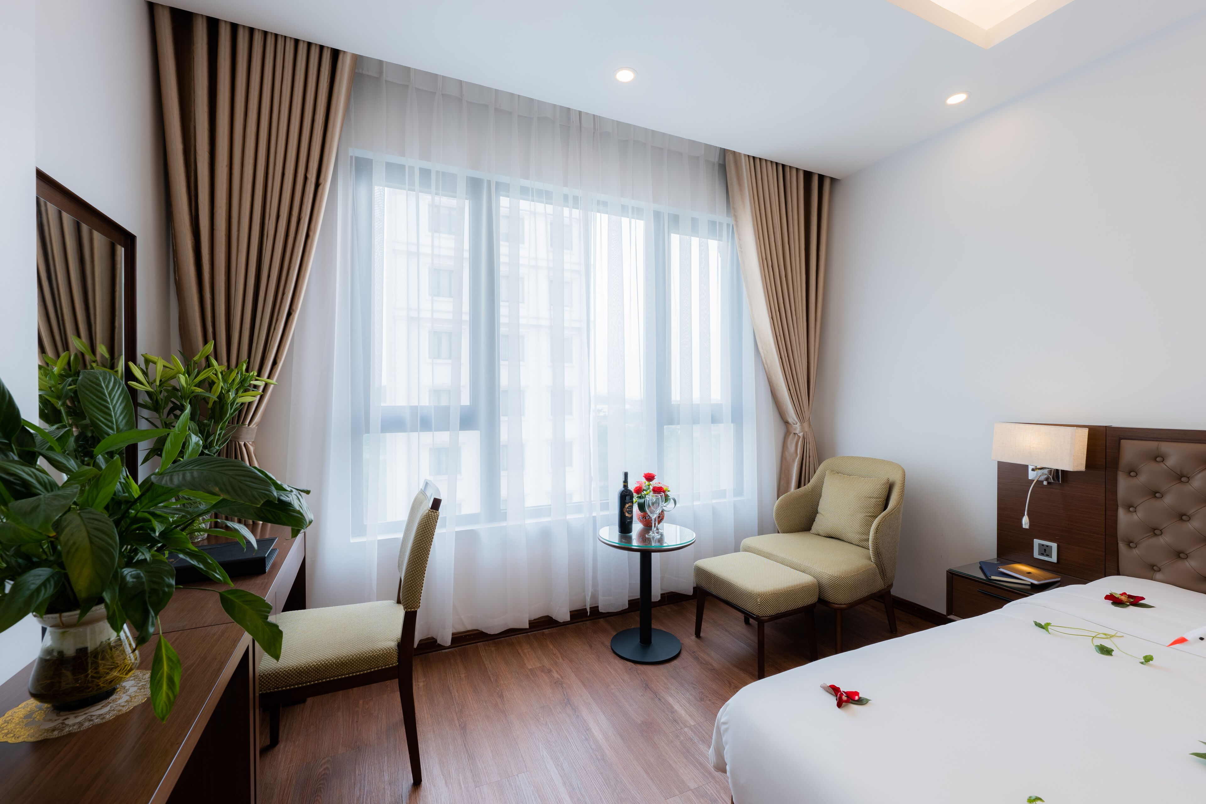 Een hotelkamer met een bed, een stoel, een kleine tafel met een bloevas en een potplant.